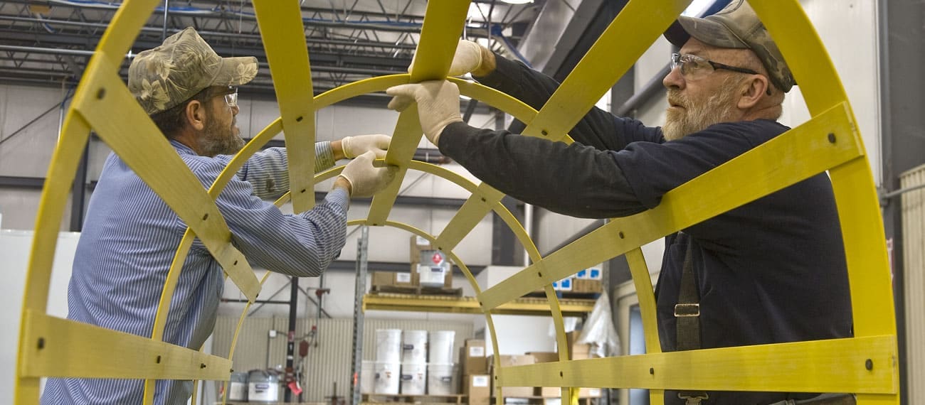Workers assembling a yellow, custom Fiberglass Reinforced Polymer safety ladder and cage system.