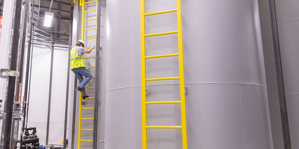 Worker in industrial plant climbing up yellow ladder attached to large vats.