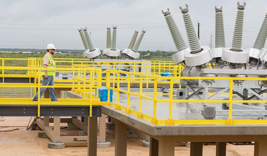 employee walking on catwalk and using railings made from yellow FRP at an electrical substation