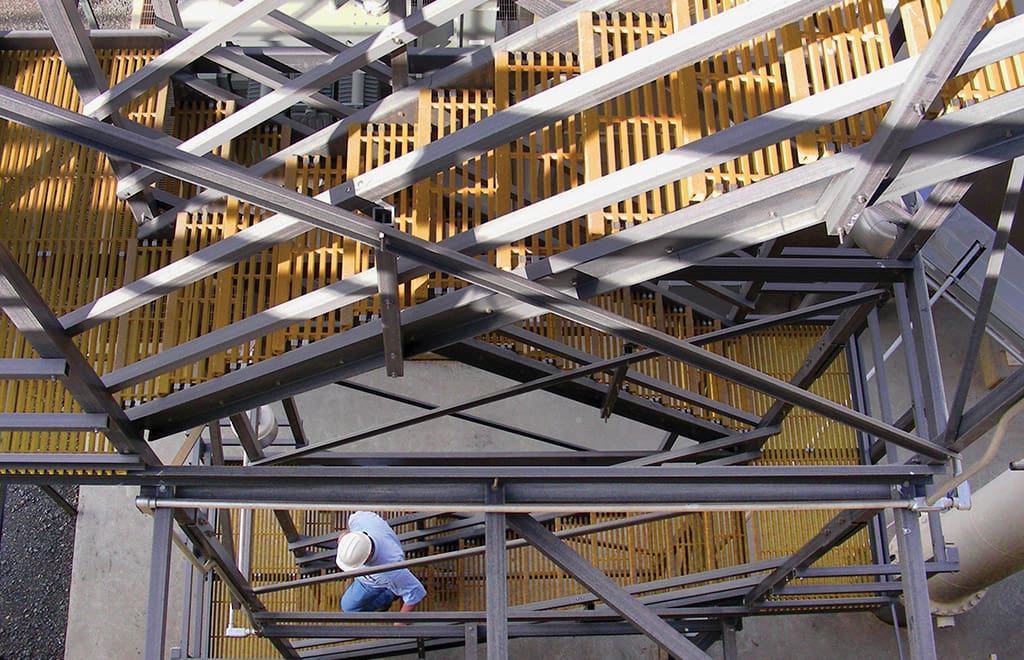 Worker in hardhat walking down a stair tower made from yellow FRP product