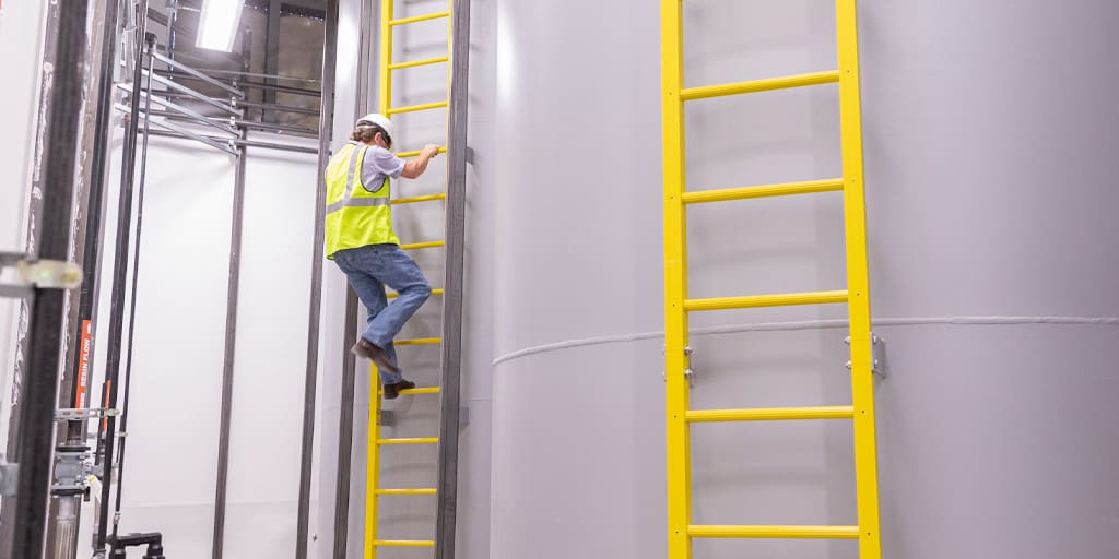 Worker scaling fiberglass reinforced plastic ladder on the side of an industrial tank.